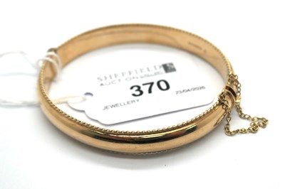 Lot 370 - A 9ct Gold Hinged Bangle, with textured edge,...